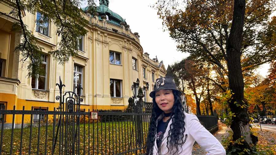 Moon Suk in elegantem Frack vor Löwenpalais Villa, Symbol für kreative Partnerschaften und Werte.