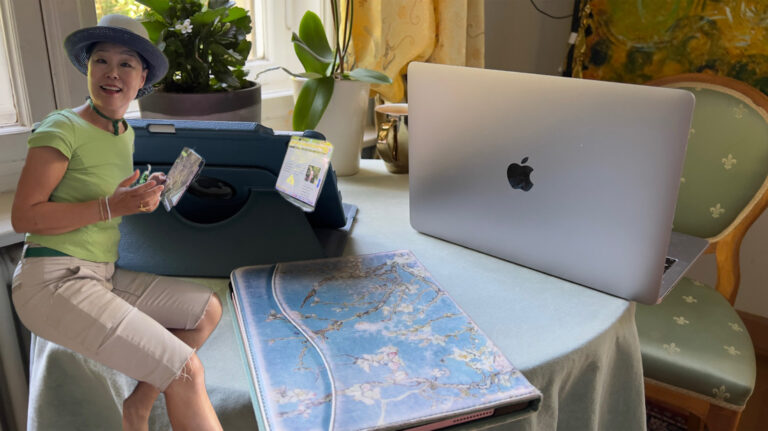 Atelierzimmer mit kleinem runden Tisch, zwei iPads, einem Mac Laptop und einem freigestellten Foto von Moon Suk neben ihren Apple-Geräten, die für die Blog-Arbeit bereitstehen.