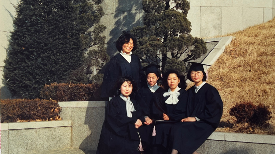Moon Suk feiert Uniabschluss mit vier Kommilitoninnen auf dem Campus in Roben und Hüten.